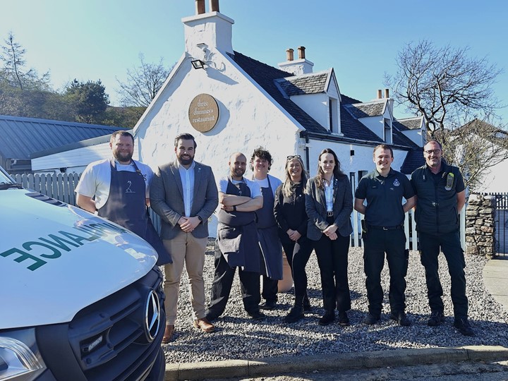 Restaurant staff stand together with Scottish Ambulance Service staff smiling in front of Three Chimneys with an ambulance in the foreground