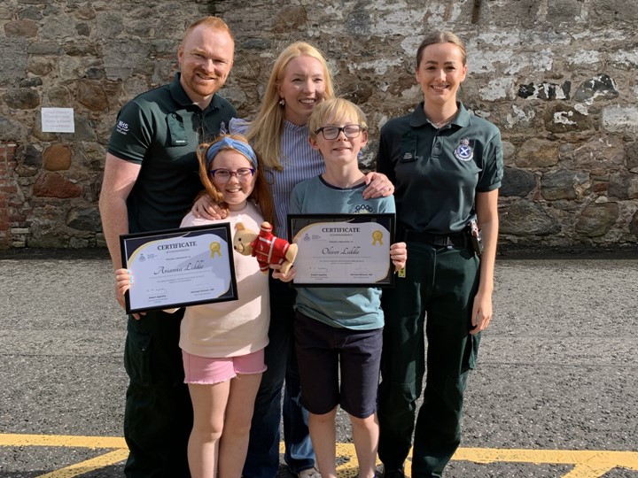 Siblings presented with their certificates by the Scottish Ambulance Service stand next to SAS staff members