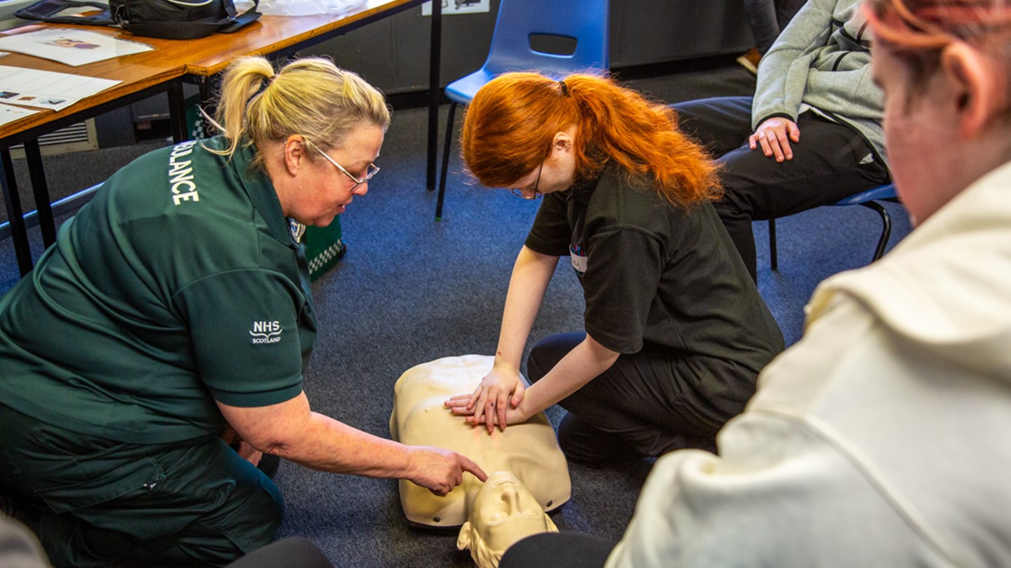 A Paramedic shows a school pupil how to perform CPR on a mannequin