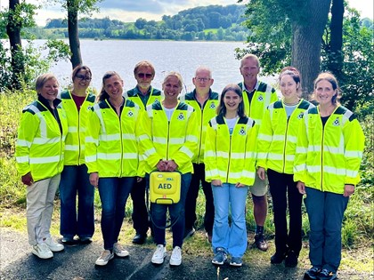 A group of 10 people in high vis jackets, one holding an AED, and smiling together